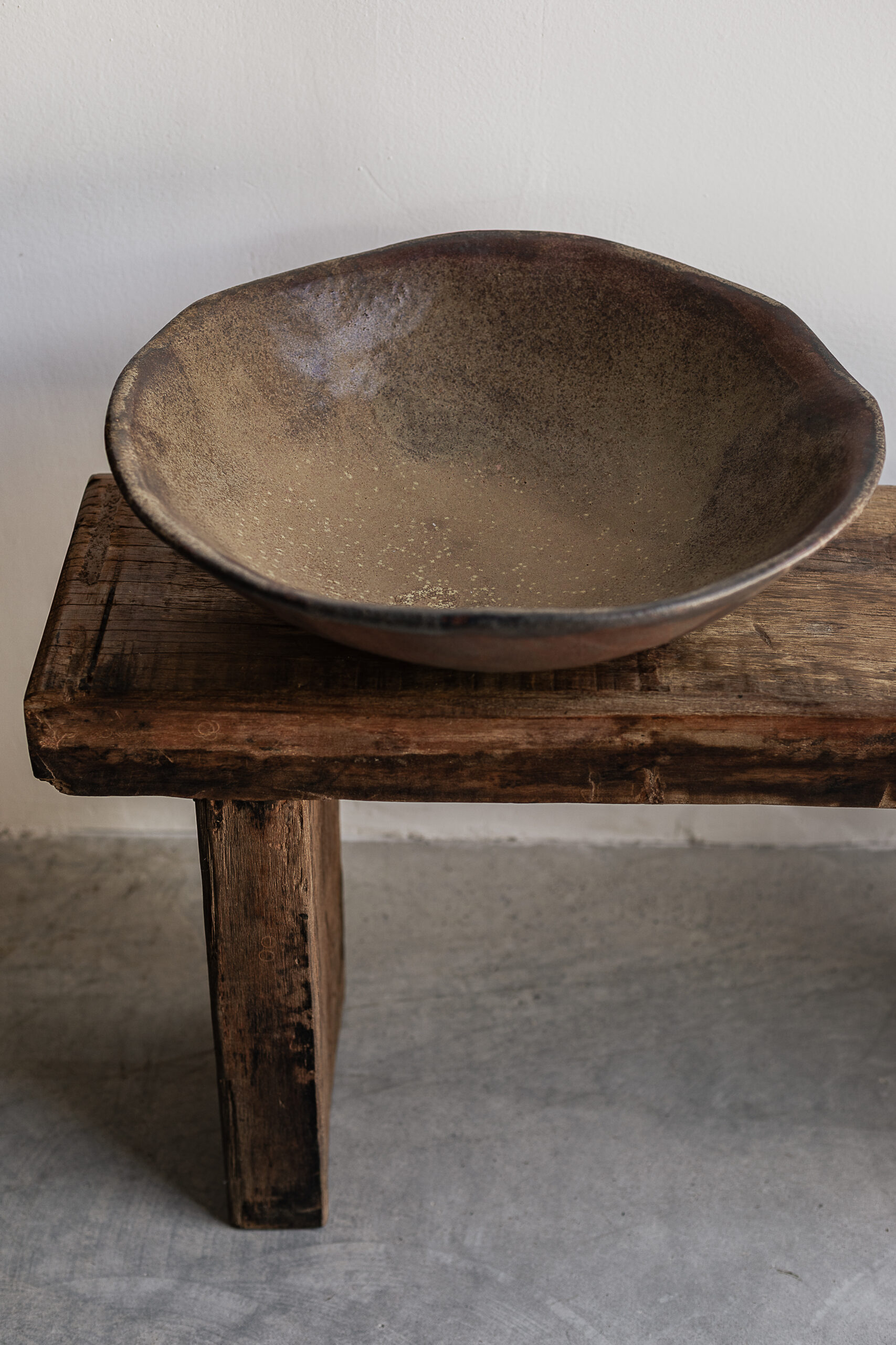 Large handmade rust brown stoneware bowl by Badass Ceramics with raw organic rim, styled on reclaimed wood bench — Soulosofie Mallorca