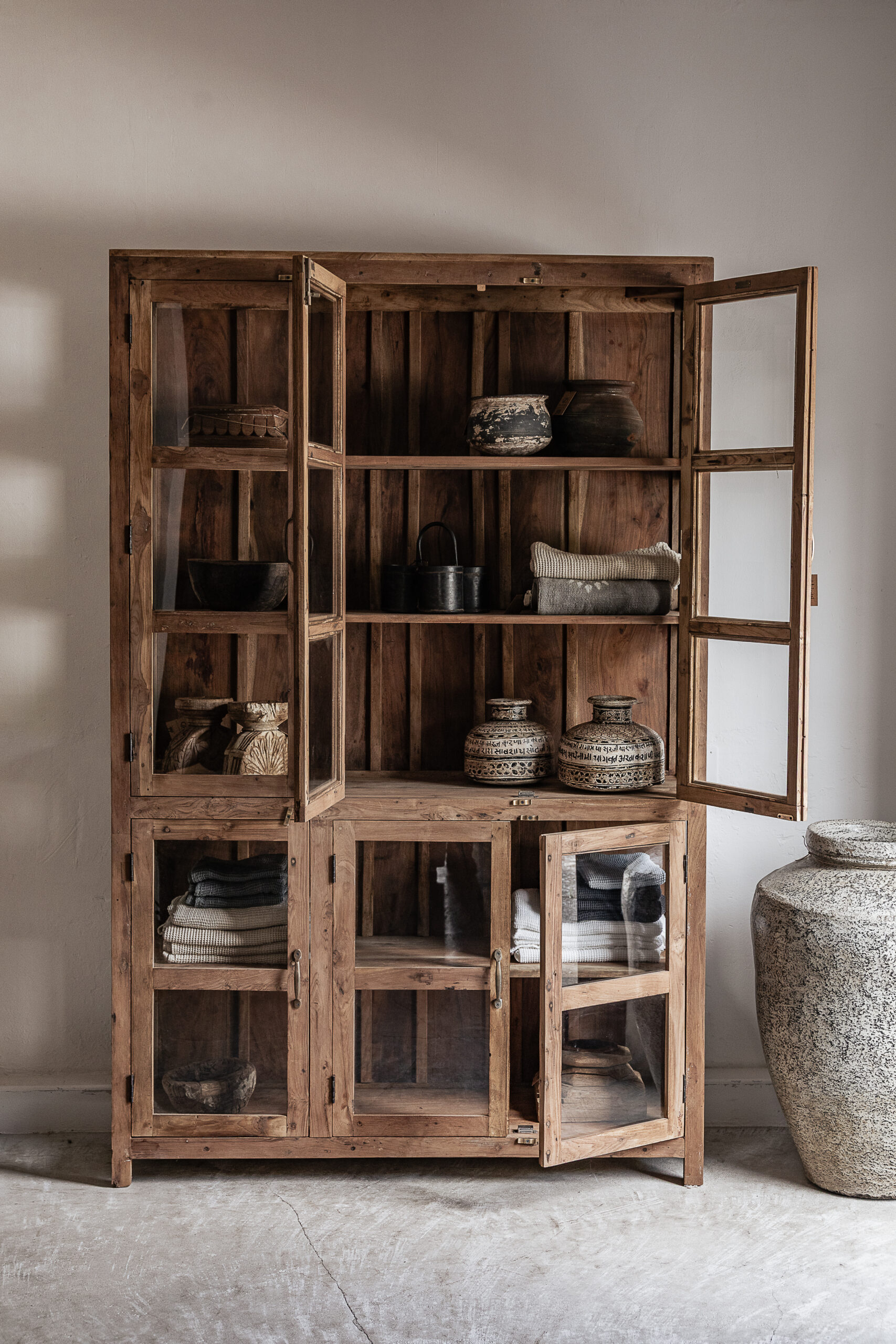 Large reclaimed teak cabinet with glass doors and open shelves, styled with vintage ceramics and textiles — Soulosofie Mallorca