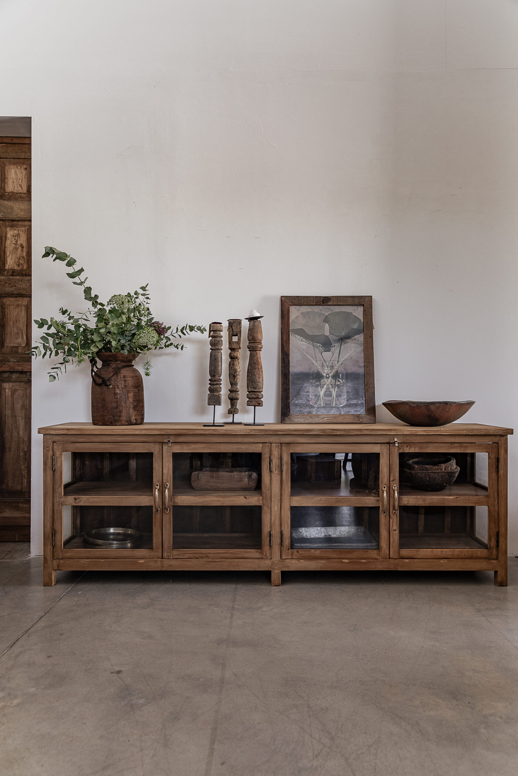 Reclaimed teak sideboard with four glass doors and open shelves, styled with vintage ceramics and eucalyptus — Soulosofie Mallorca