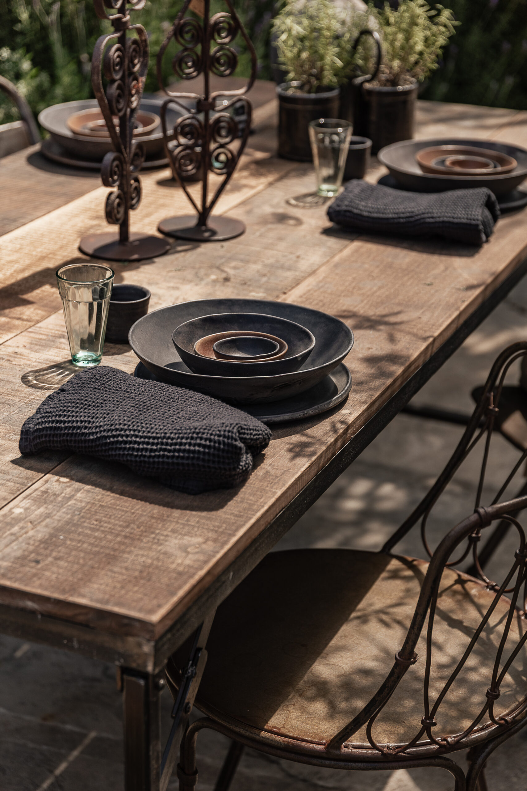 Reclaimed wood outdoor dining table with rustic iron legs, styled with handmade dark ceramics and black linen napkins — Soulosofie Mallorca