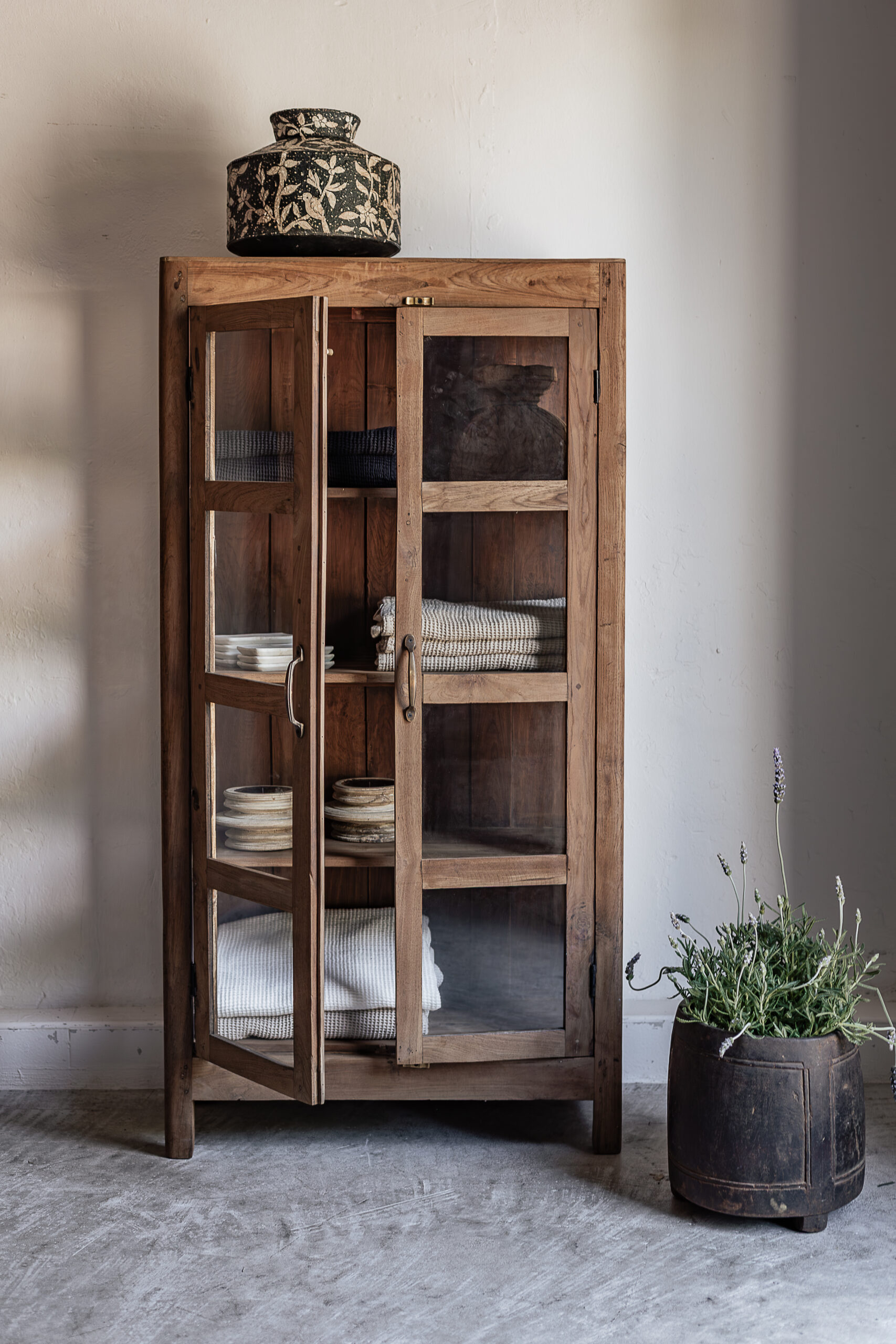Vintage teak narrow glass door display cabinet with open shelves, styled with folded linen textiles and ceramics — Soulosofie Mallorca
