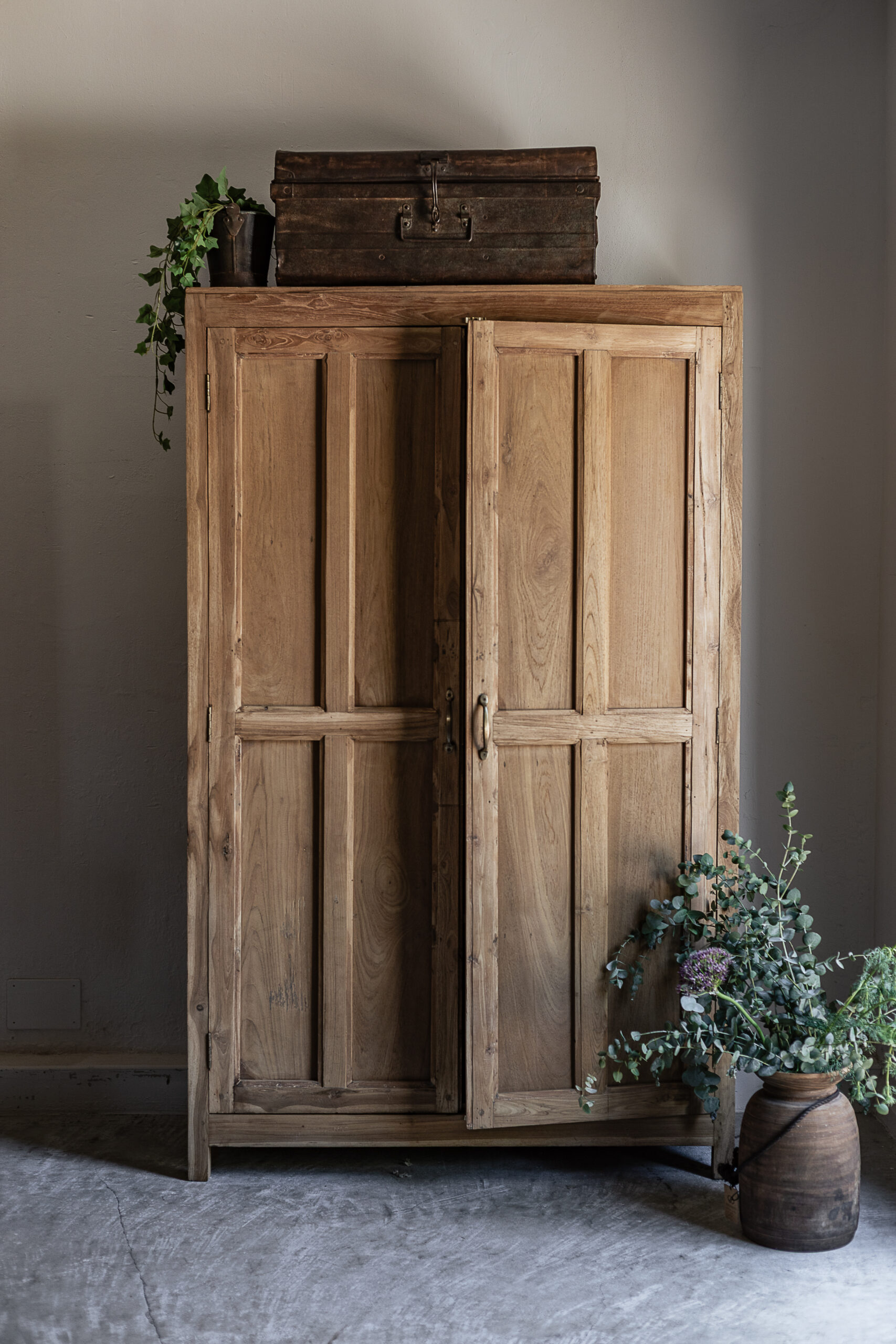 Vintage teak wardrobe with solid panel doors and brass handle, styled with vintage trunk and eucalyptus — Soulosofie Mallorca